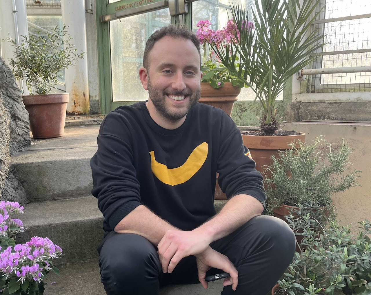 Image of Aaron Sandel smiling, sitting on a step, wearing a black long sleeve shirt with an image of a banana on it.